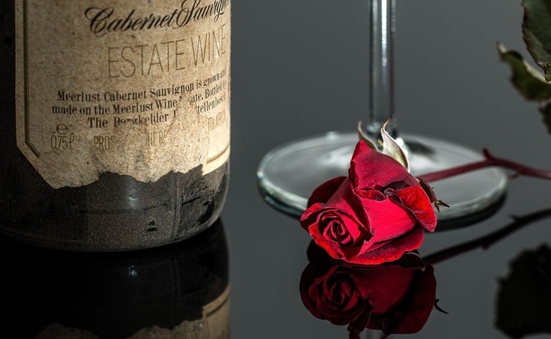 Flaša vina pored koje se nalazi ruža.