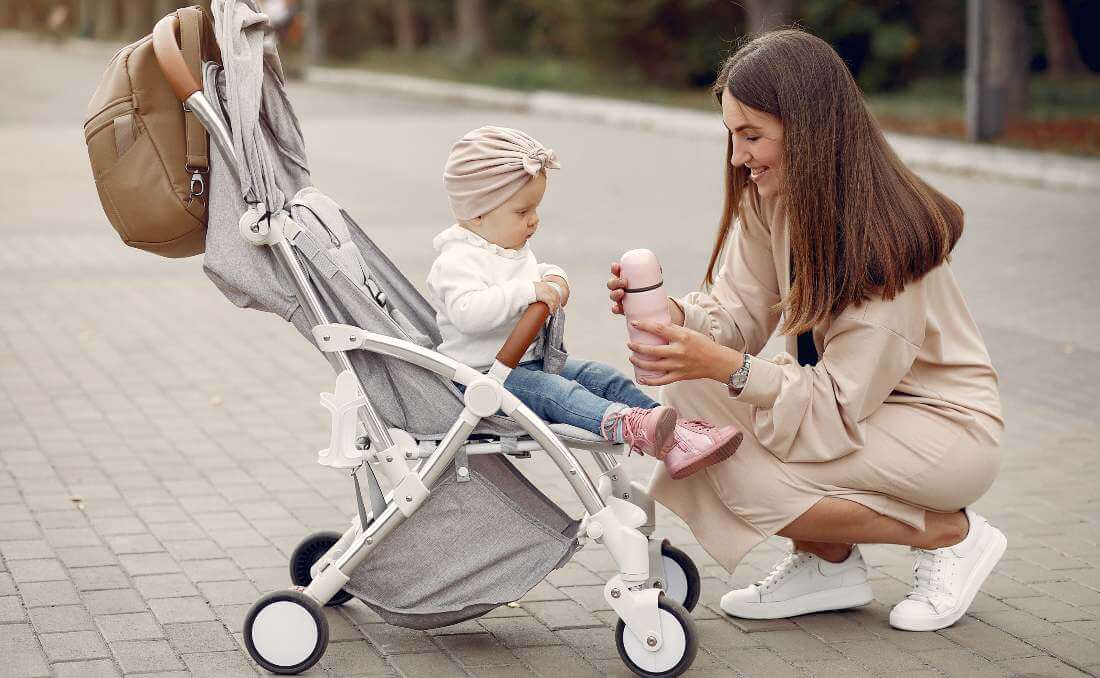 Majka daje termos bebi u kolicima