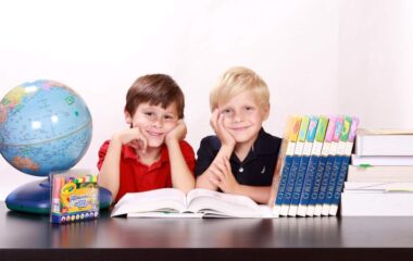 Dečaci koji su prvaci i sede za stolon pored knjiga i globusa.