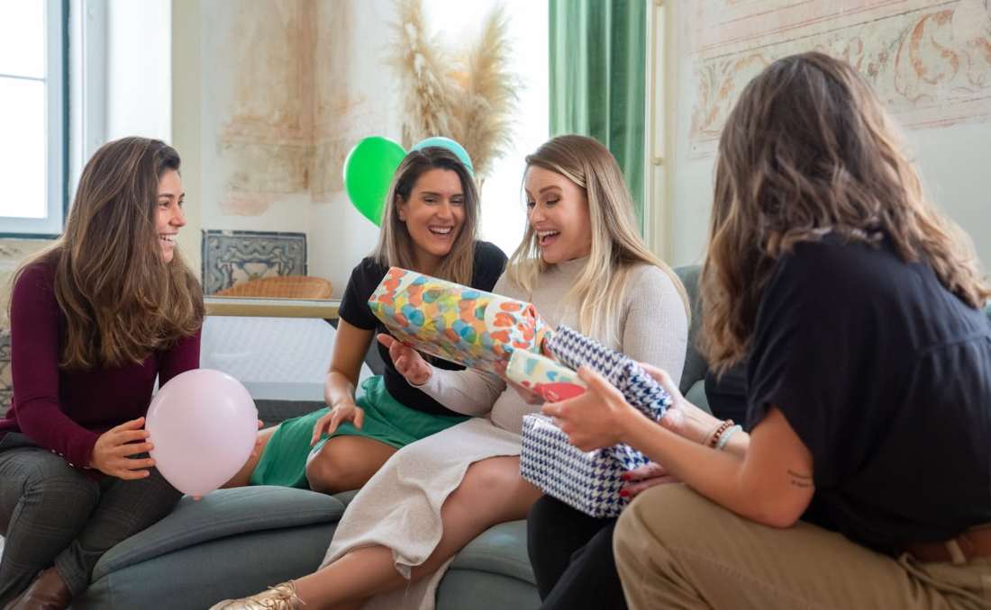 Tri devojke na kauču daju trudnici poklone.