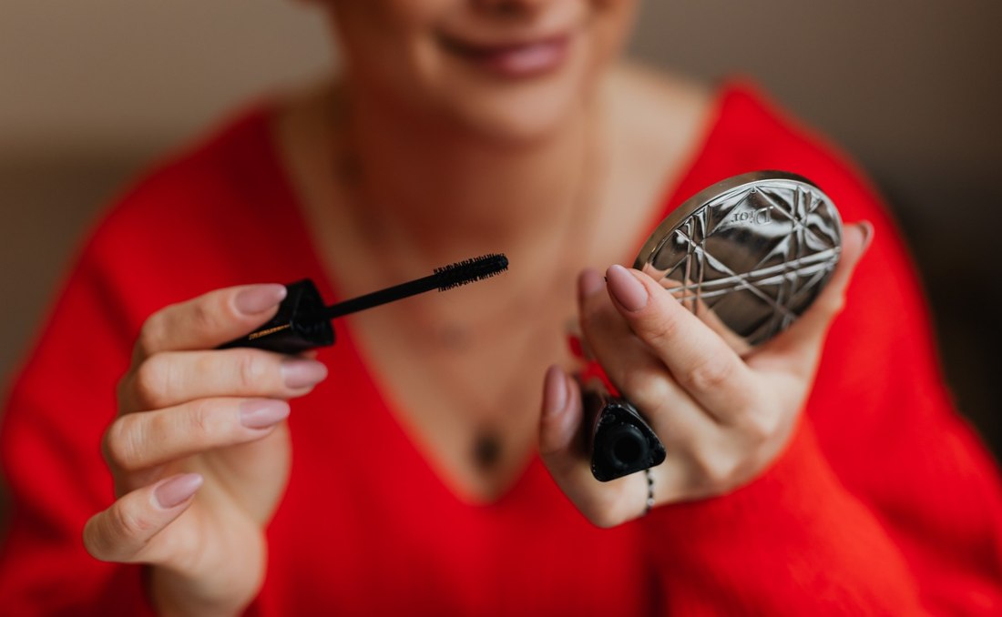 Žena u crvenoj bluzi koja stavlja maskaru.