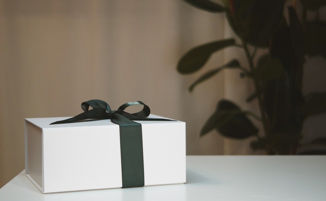 Poklon za slavu u beloj kutiji sa crnom mašnom na stolu.