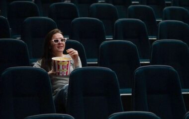 Žena koja sa osmehom gleda komediju u bioskopu i jede kokice.