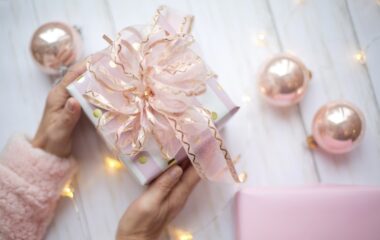 Lepo upakovan poklon u roze boji sa roze mašnom pored ukrasa.