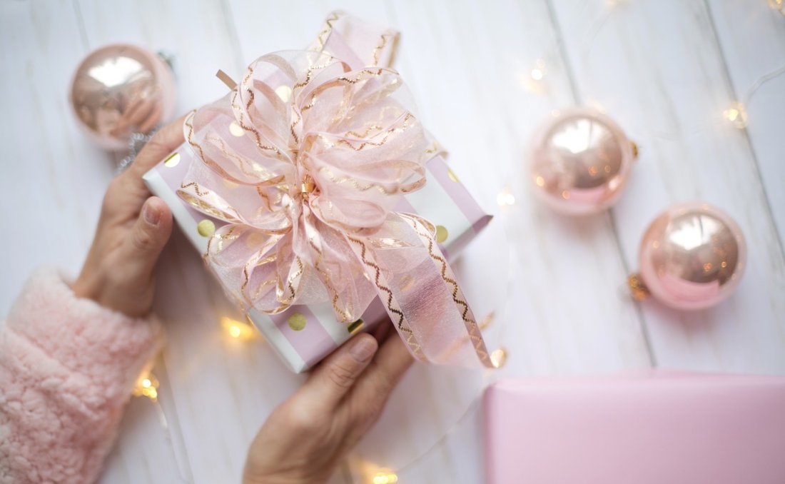 Lepo upakovan poklon u roze boji sa roze mašnom pored ukrasa.