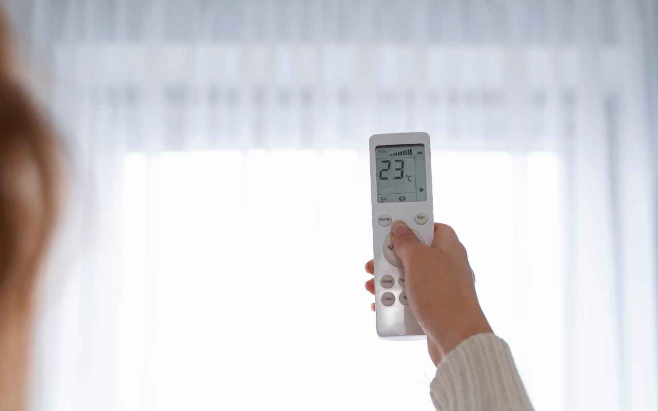 Devojka pode&scaron;ava temperaturu pomoću daljinskog upravljača za klimu.