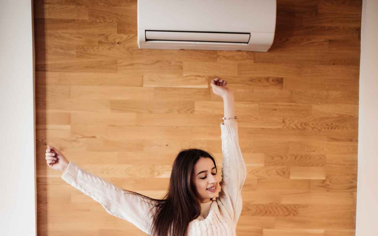 Devojka stoji na krevetu dok inverter klima uređaj hladi prostor.