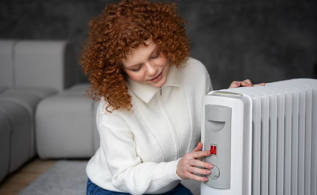 Devojka uključuje električnu grejalicu.