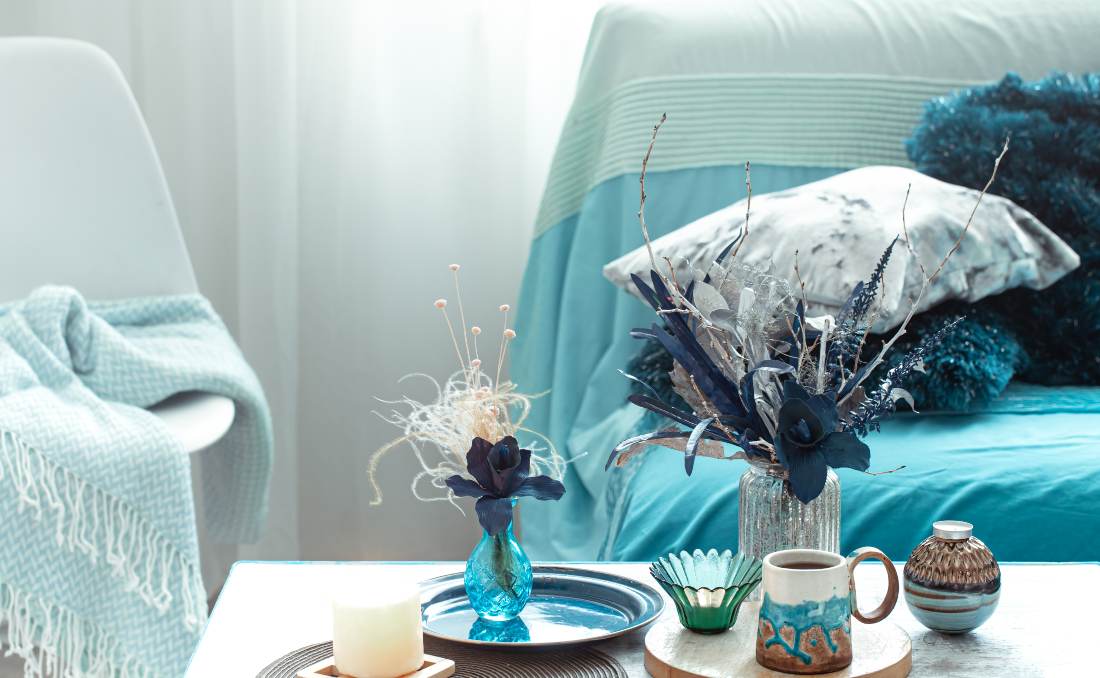 Drveni sto u dnevnoj sobi ukra&scaron;en vazom sa ve&scaron;tačkim cvećem i modernim dekoracijama.