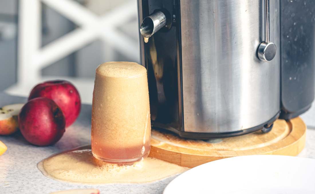 Ča&scaron;a sveže ceđenog soka pored sokovnika na kuhinjskom stolu.