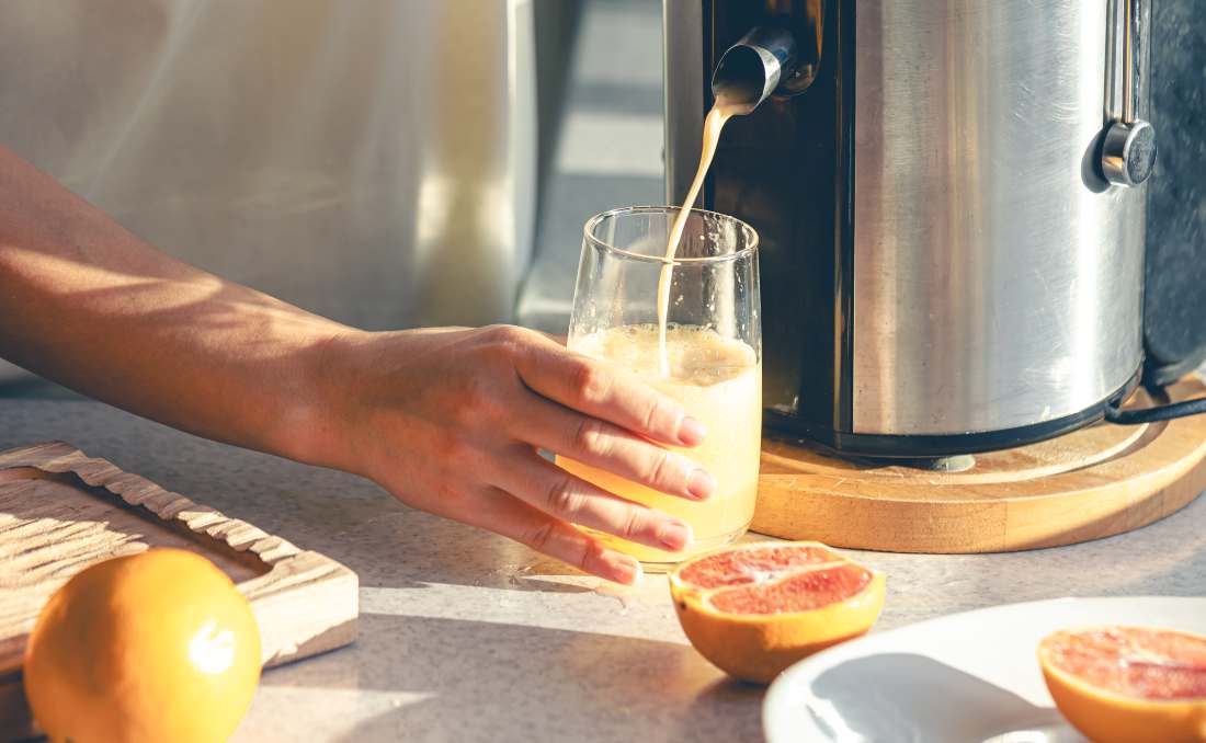 Čovek priprema svež sok pomoću električnog sokovnika u kuhinji.