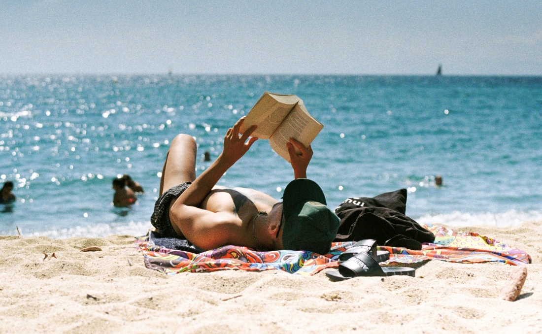 Muškarac leži na plaži i čita knjigu.
